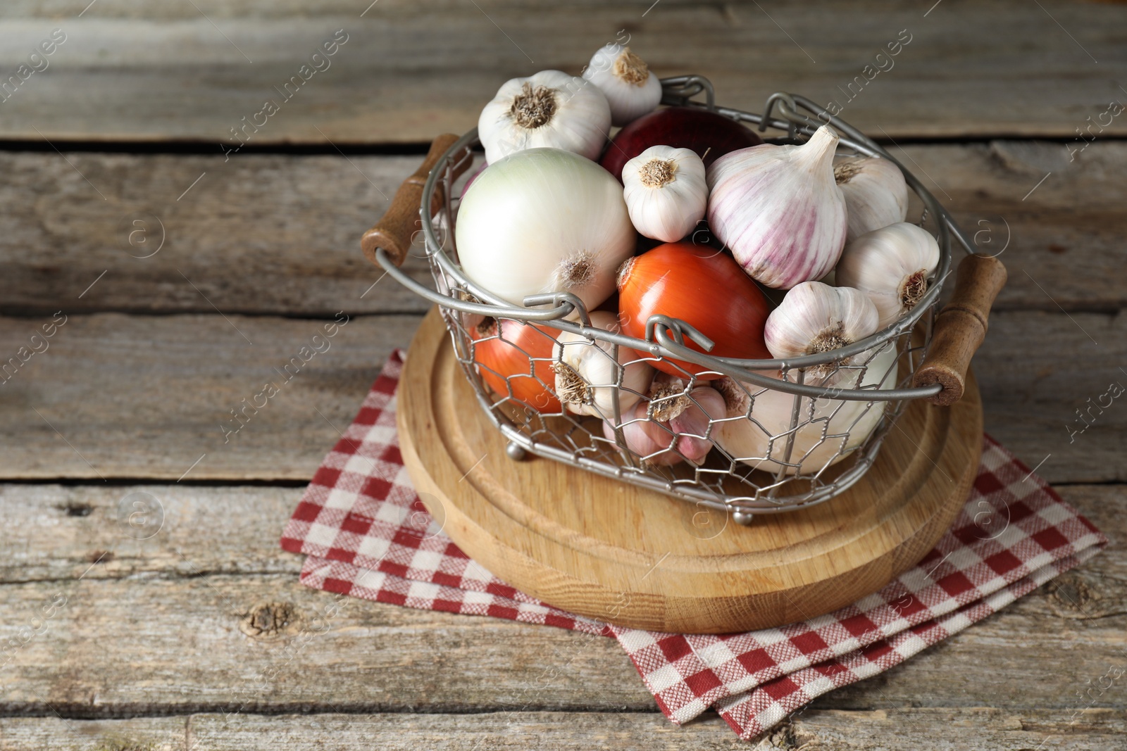 Photo of Fresh raw garlic and onions in metal basket on wooden table. Space for text