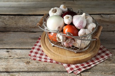 Photo of Fresh raw garlic and onions in metal basket on wooden table. Space for text