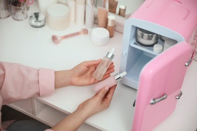 Photo of Woman taking cosmetic products out of mini refrigerator indoors, closeup