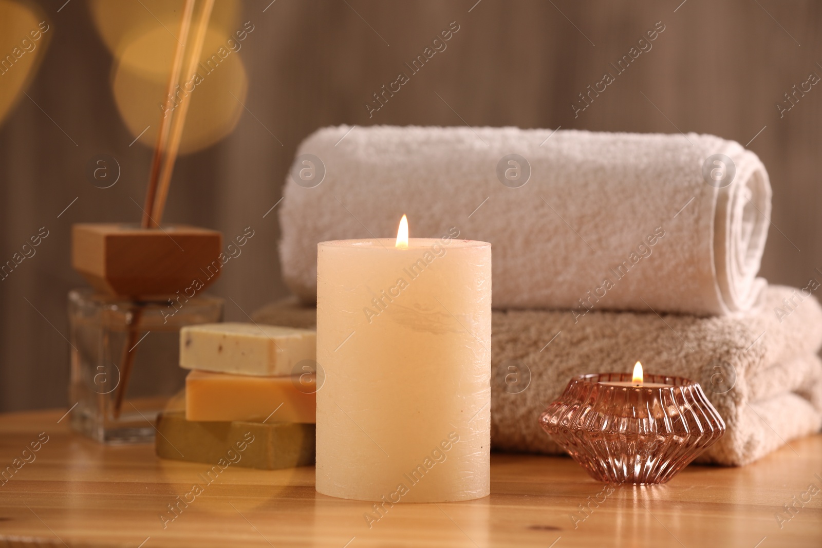 Photo of Spa composition. Burning candles, towels, soap and reed air freshener on wooden table, closeup