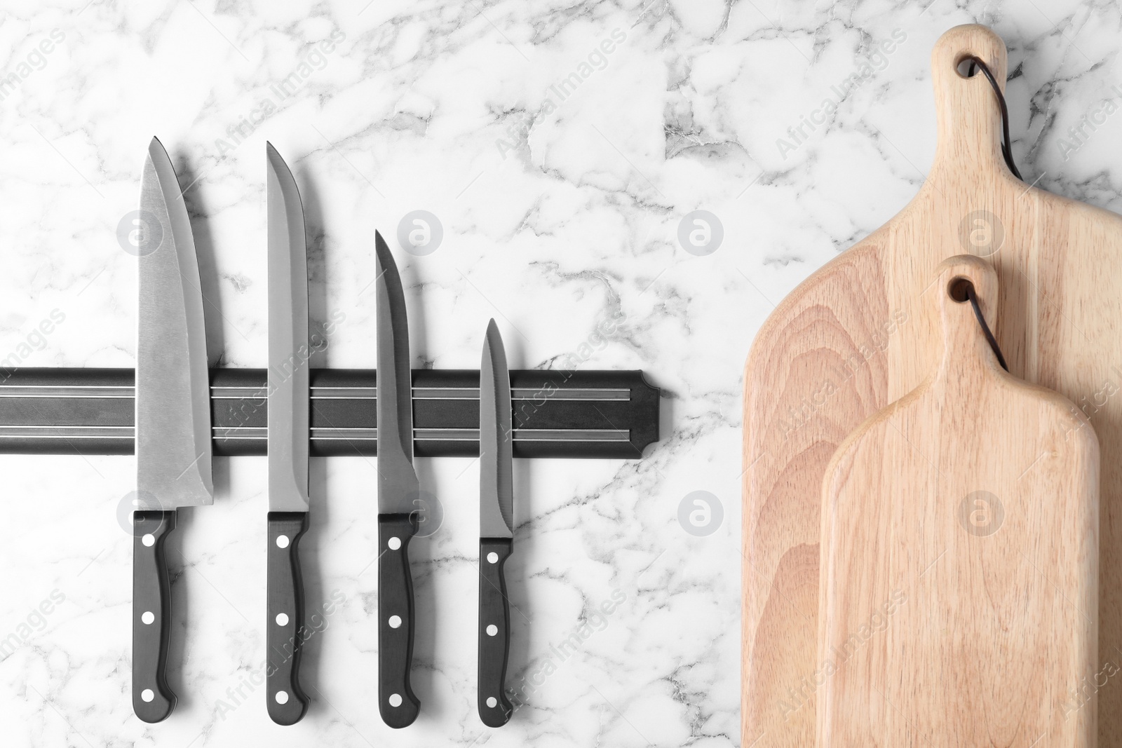 Photo of Magnetic holder with set of knives and wooden boards against marble background