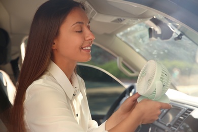 Photo of Young woman enjoying air flow from portable fan in car on hot summer day