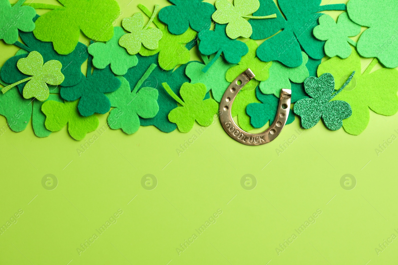 Photo of Flat lay composition with clover leaves and horseshoe on green background, space for text. St. Patrick's day