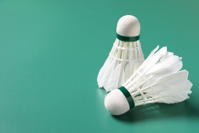 Feather badminton shuttlecocks on green background, closeup. Space for text