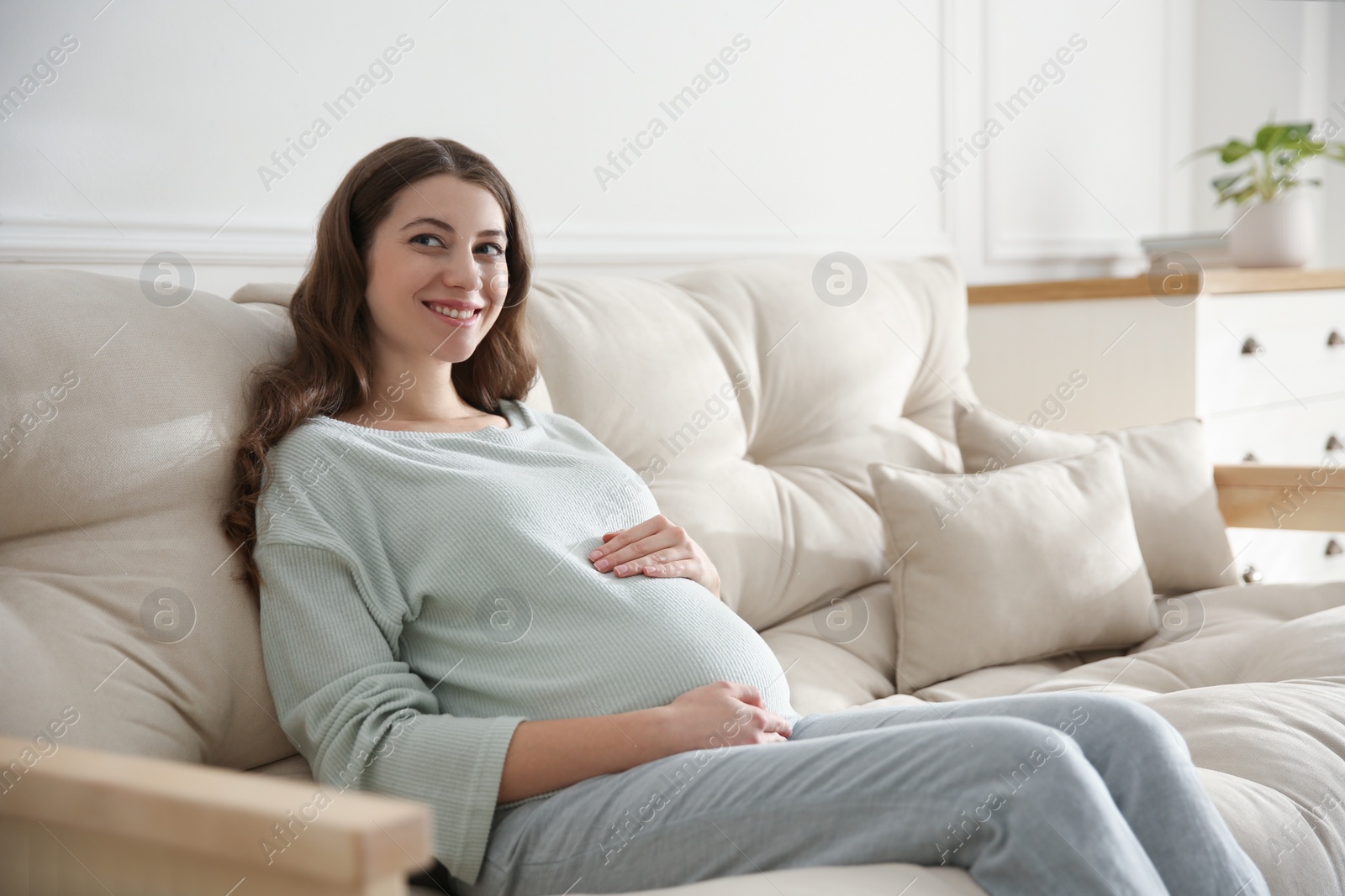 Photo of Happy pregnant woman touching her belly indoors