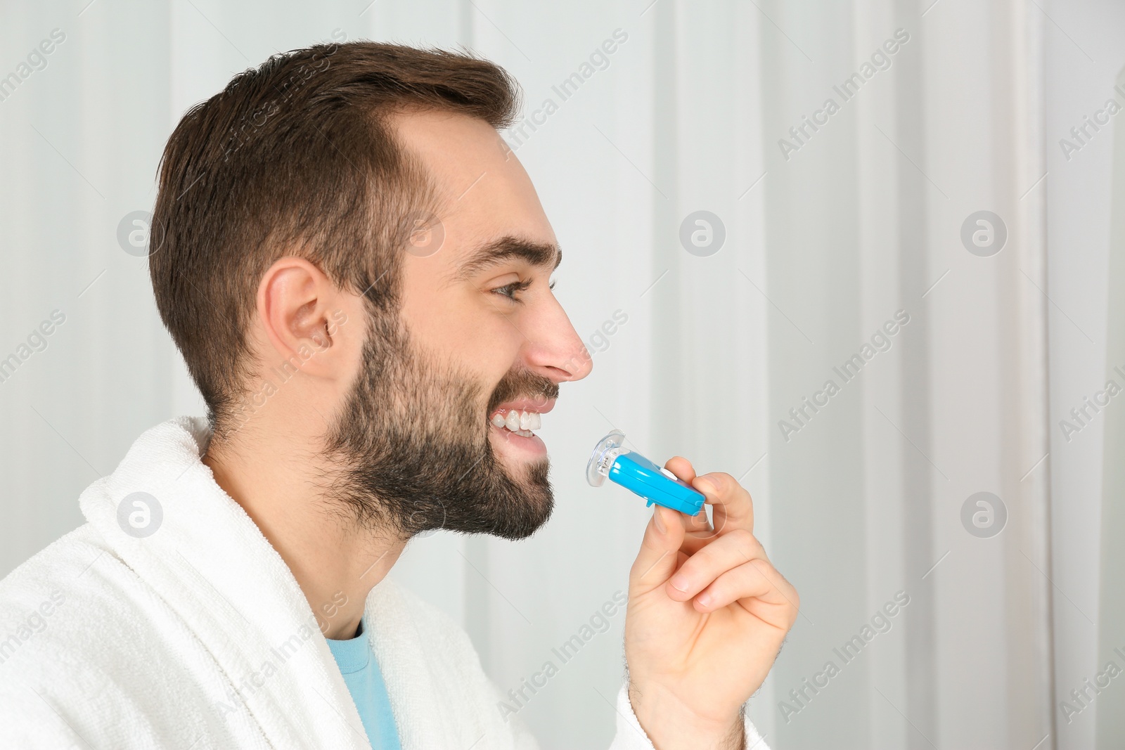 Photo of Young man using teeth whitening device on light background. Space for text