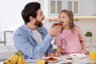 Father and his cute little daughter having breakfast at table in kitchen