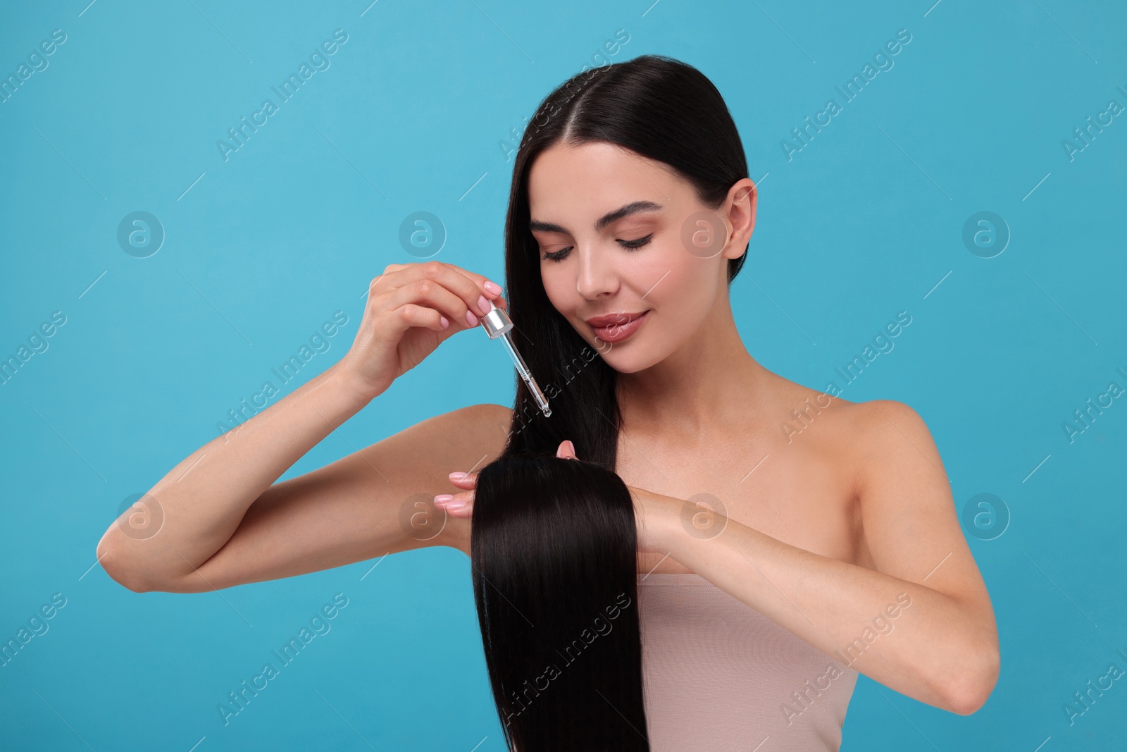 Photo of Beautiful woman applying hair serum on light blue background. Cosmetic product