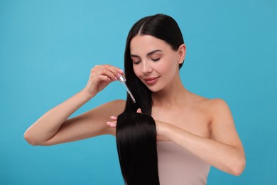 Beautiful woman applying hair serum on light blue background. Cosmetic product