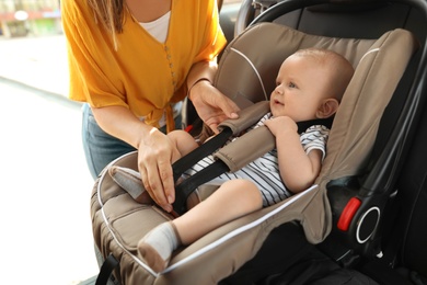 Mother fastening baby to child safety seat inside of car