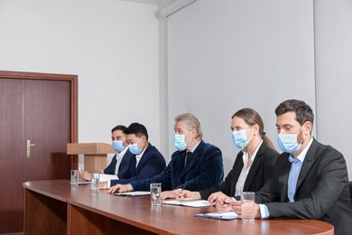 Photo of Business conference. People with protective masks working at table in meeting room