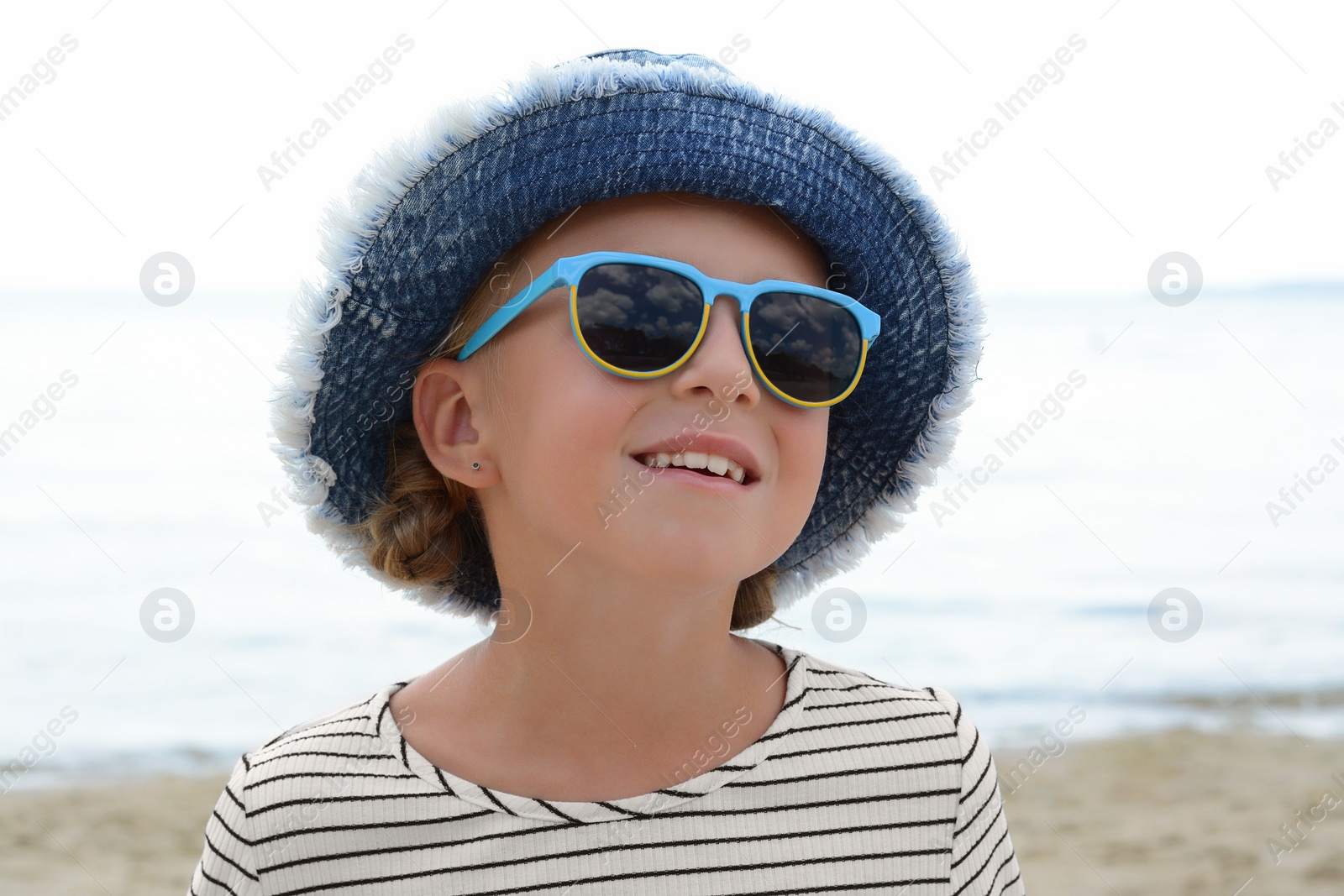 Photo of Little girl wearing sunglasses and hat at beach on sunny day