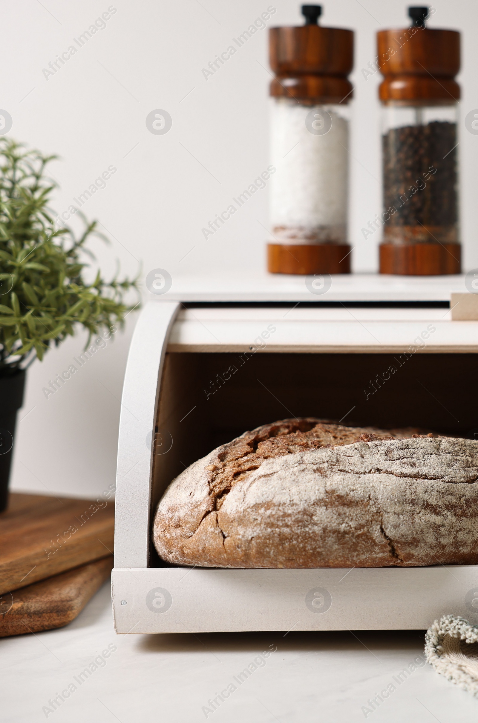 Photo of Wooden bread basket with freshly baked loaves on white marble table in kitchen