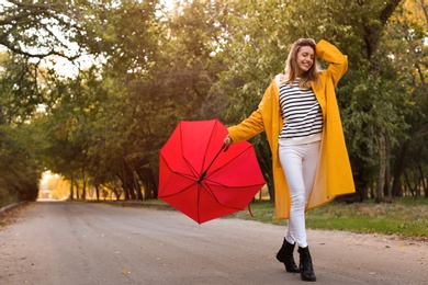 Photo of Beautiful young woman wearing stylish autumn clothes with red umbrella in park