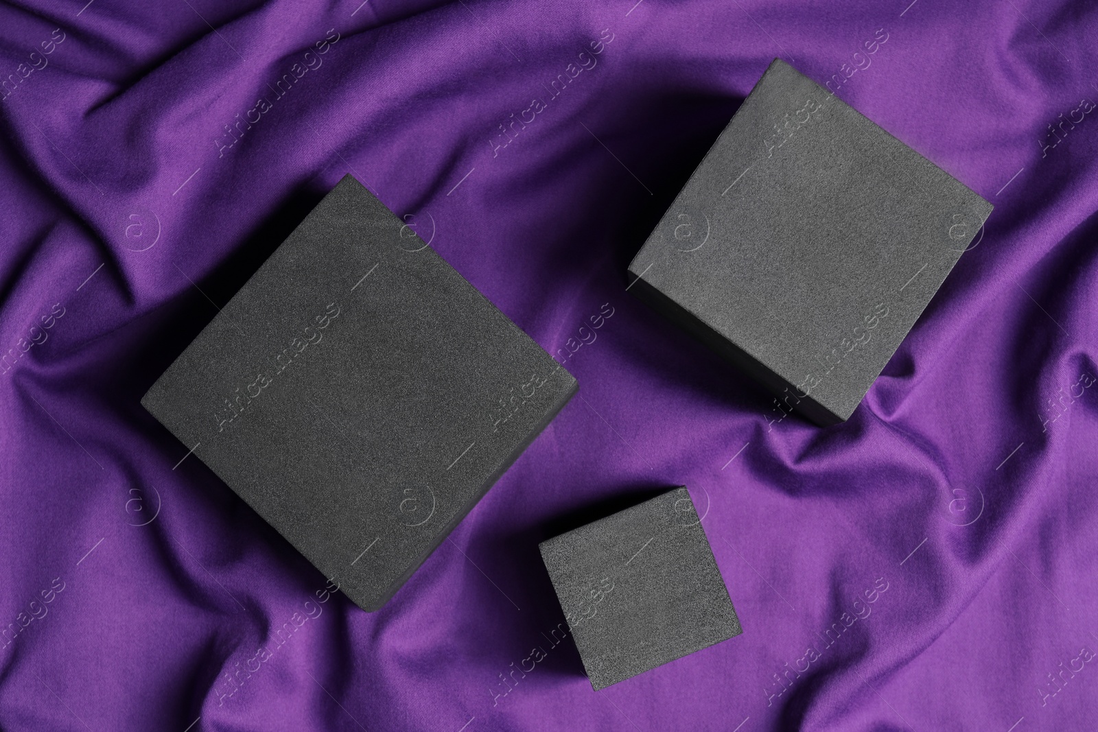 Photo of Black cubes on purple fabric, flat lay. Stylish presentation for product