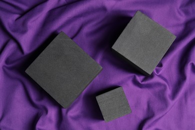 Black cubes on purple fabric, flat lay. Stylish presentation for product