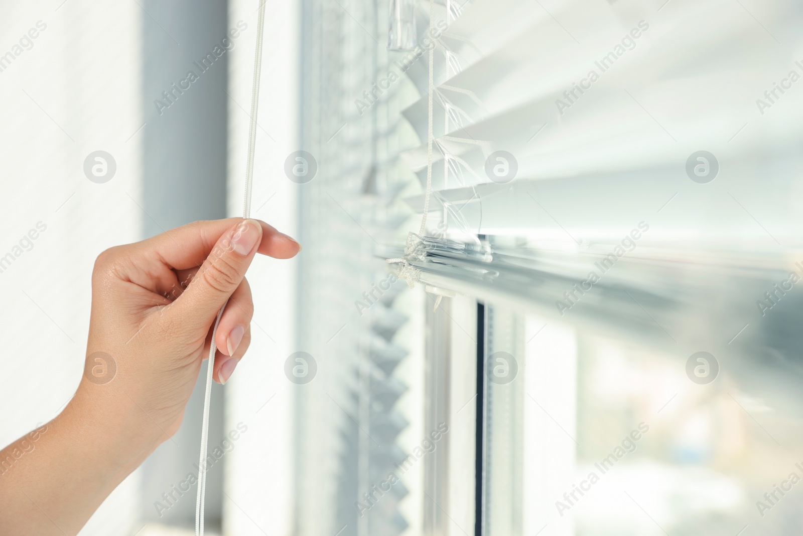 Photo of Woman opening horizontal blinds on window indoors, closeup