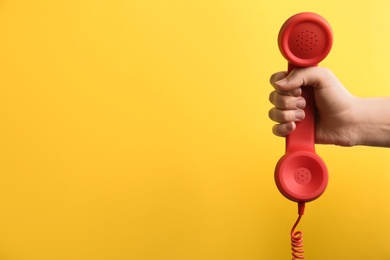Photo of Closeup view of woman holding red corded telephone handset on yellow background, space for text. Hotline concept