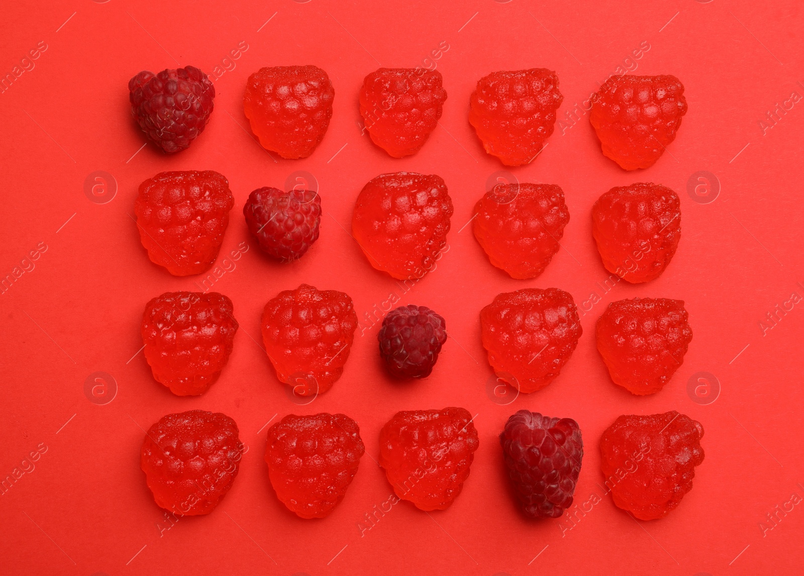 Photo of Delicious gummy candies and fresh raspberries on red background, flat lay