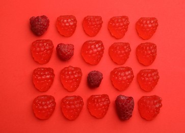 Photo of Delicious gummy candies and fresh raspberries on red background, flat lay