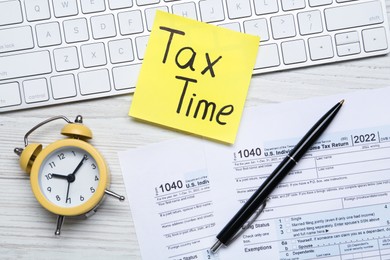 Photo of Reminder note with words Tax Time, documents, computer keyboard and alarm clock on white wooden table, flat lay