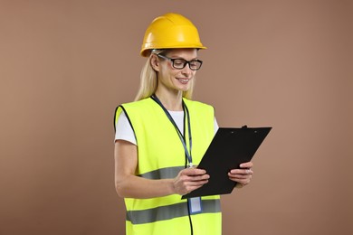 Engineer in hard hat holding clipboard on brown background