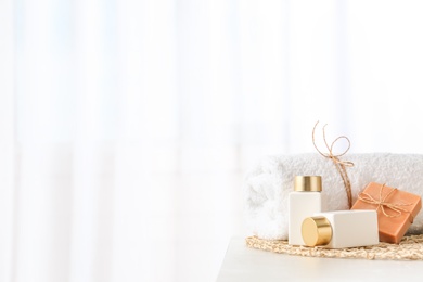 Cosmetic bottles, handmade soap and towel on light grey table indoors, space for text. Spa treatment