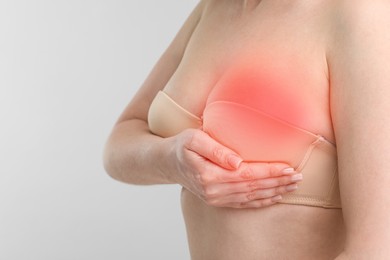 Young woman suffering from breast pain on light background, closeup