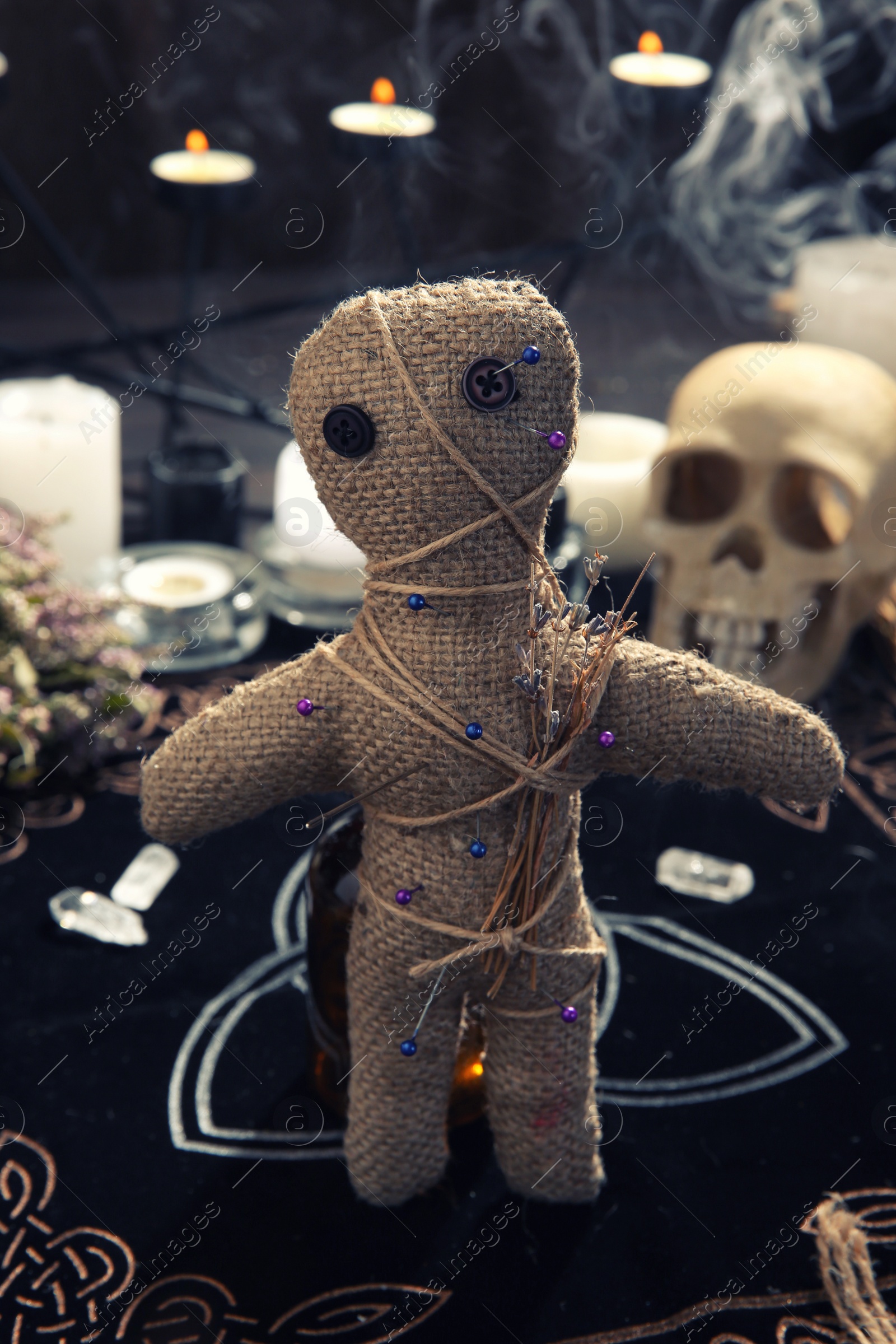 Photo of Voodoo doll with pins and dried flowers on table indoors