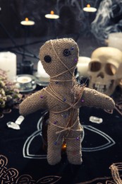 Voodoo doll with pins and dried flowers on table indoors