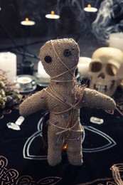 Photo of Voodoo doll with pins and dried flowers on table indoors