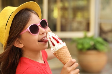 Cute little girl with delicious ice cream in park, space for text