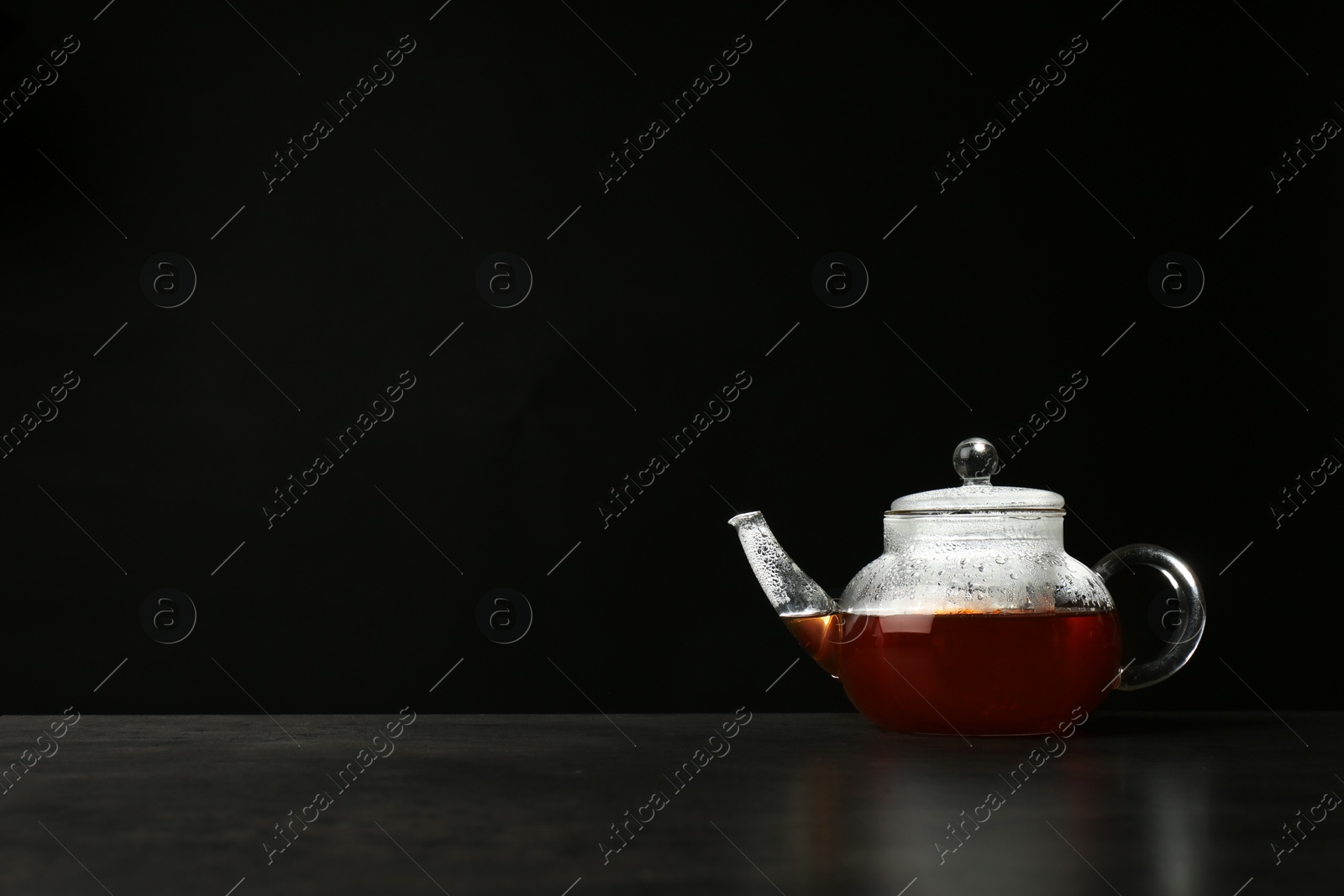 Photo of Glass teapot with delicious hot beverage on table against dark background. Space for text