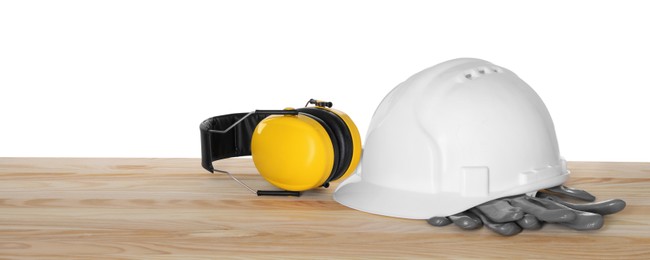 Hard hat, earmuffs and gloves on wooden table against white background. Safety equipment