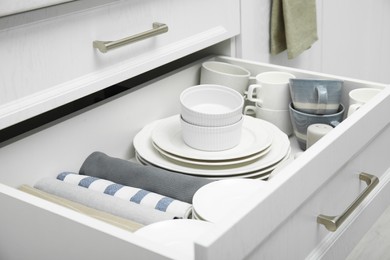 Photo of Open drawerkitchen cabinet with different dishware and towels, closeup