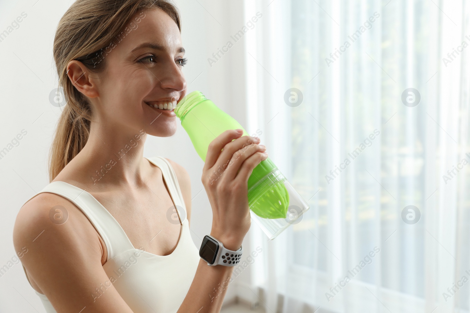 Photo of Young woman with smart watch drinking water indoors, space for text