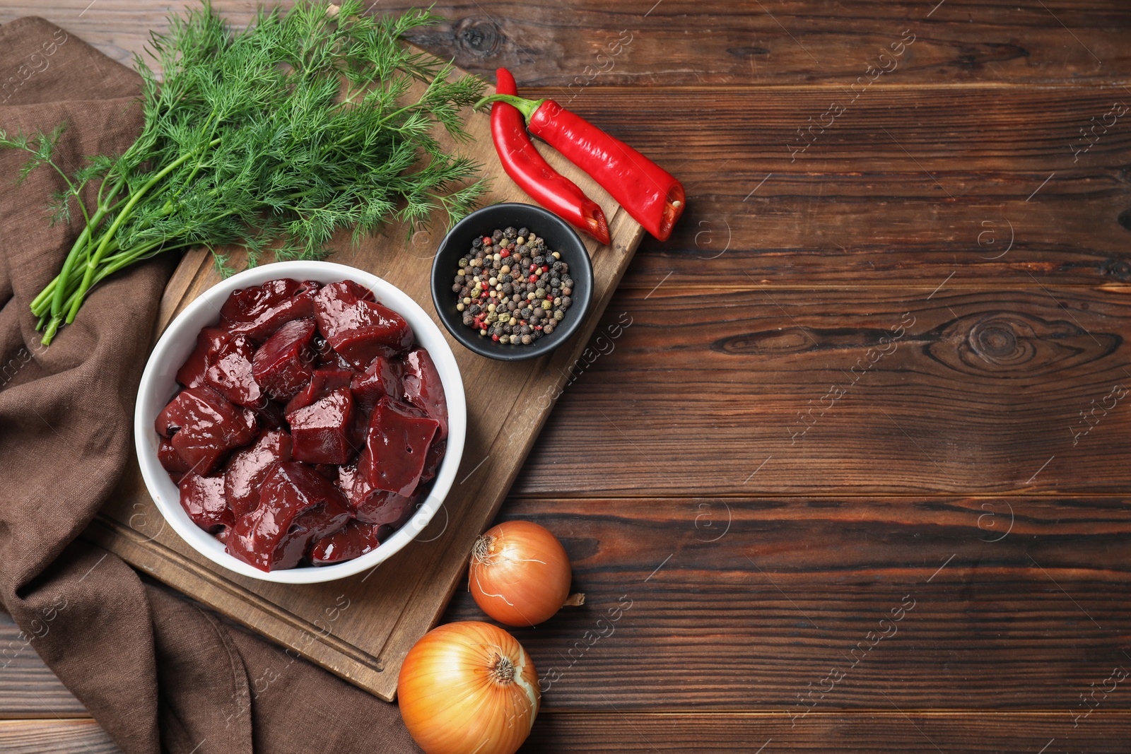 Photo of Cut raw beef liver with onions, spices, chili peppers and dill on wooden table, flat lay. Space for text