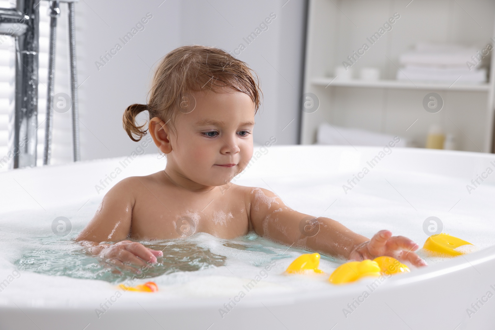 Photo of Cute little girl with rubber ducks in foamy bath at home