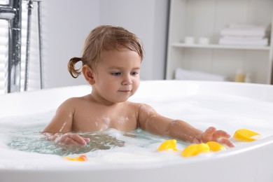 Photo of Cute little girl with rubber ducks in foamy bath at home