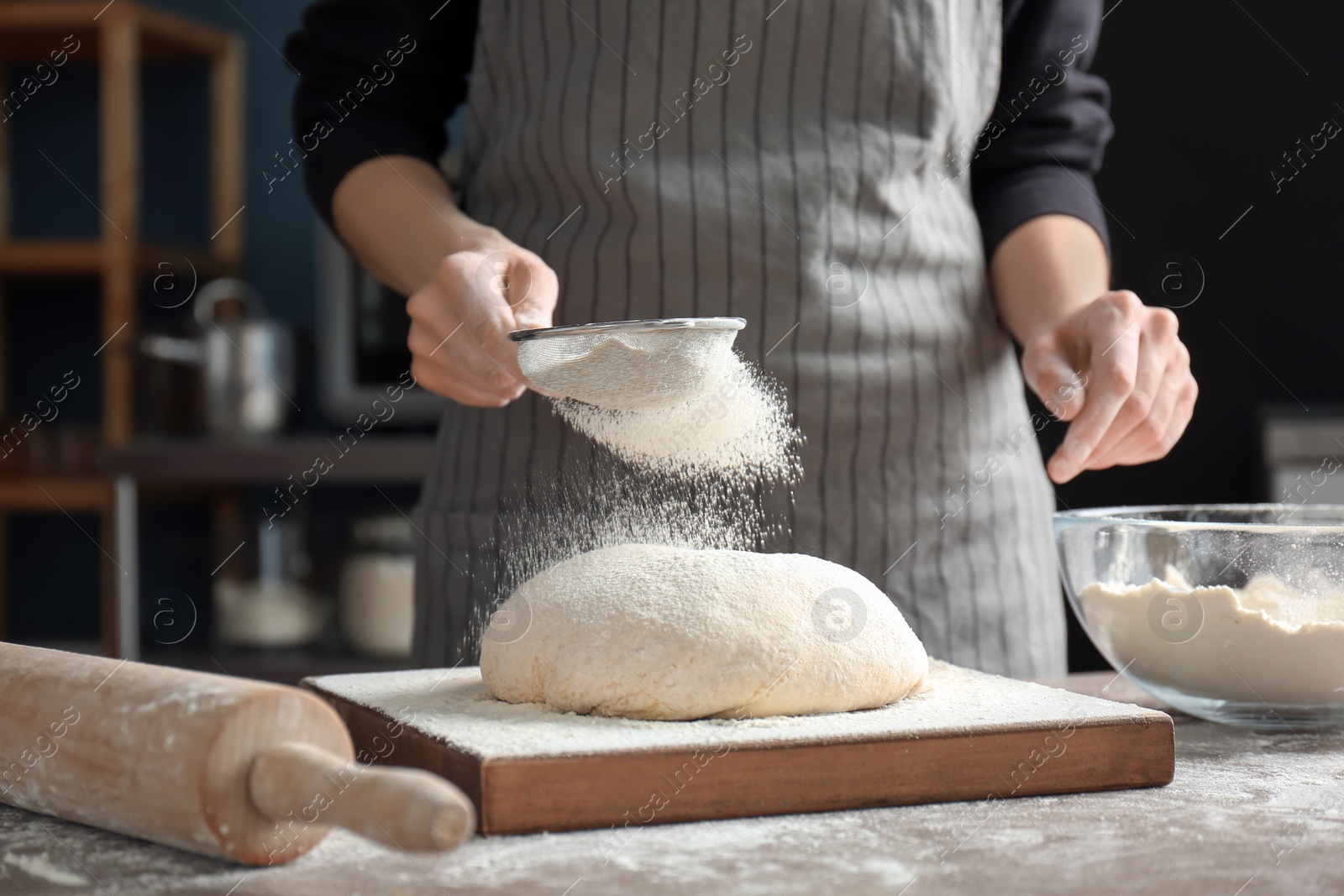 Photo of Woman sprinkling flour over dough on table in kitchen