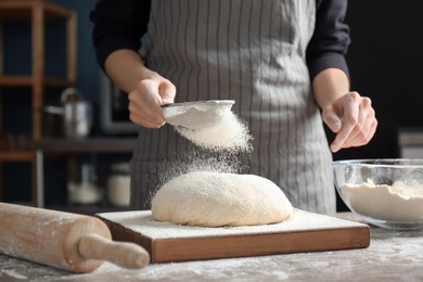 Woman sprinkling flour over dough on table in kitchen