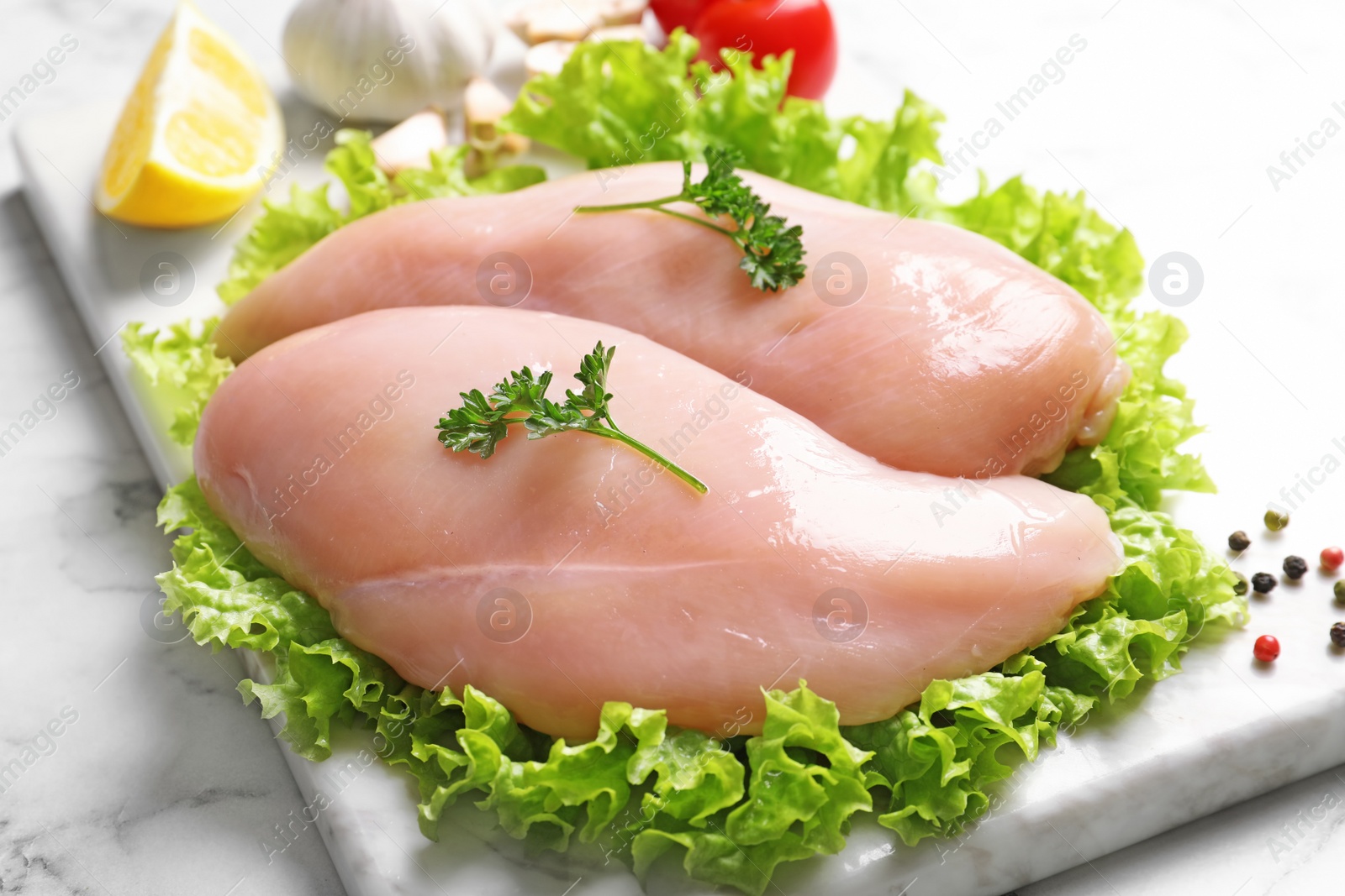 Photo of Board with raw chicken breasts and lettuce on marble table