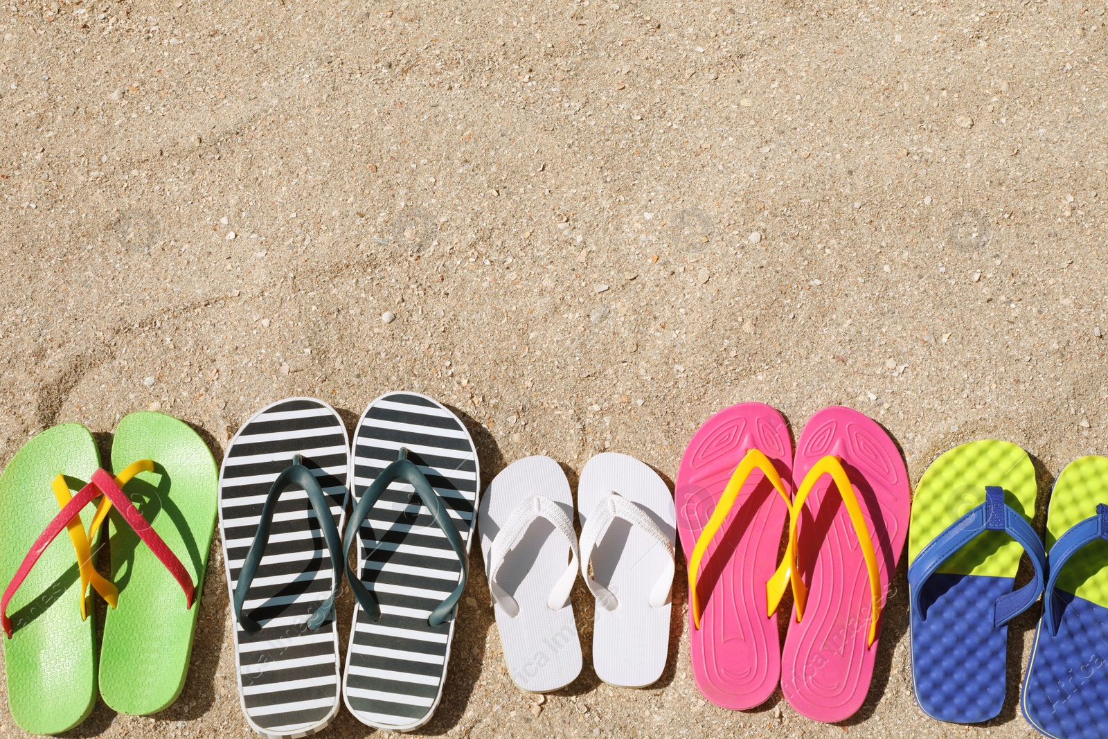 Photo of Many different flip flops on sand, flat lay. Space for text