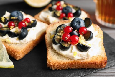 Photo of Tasty sandwiches with cream cheese, blueberries, red currants and lemon zest on slate plate, closeup
