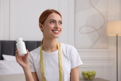 Happy young woman with bottle of pills and measuring tape at home, space for text. Weight loss