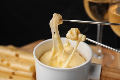 Photo of Pot of tasty cheese fondue and forks with bread on table against black background