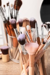 Photo of Set of professional makeup brushes and mirror on wooden table, closeup