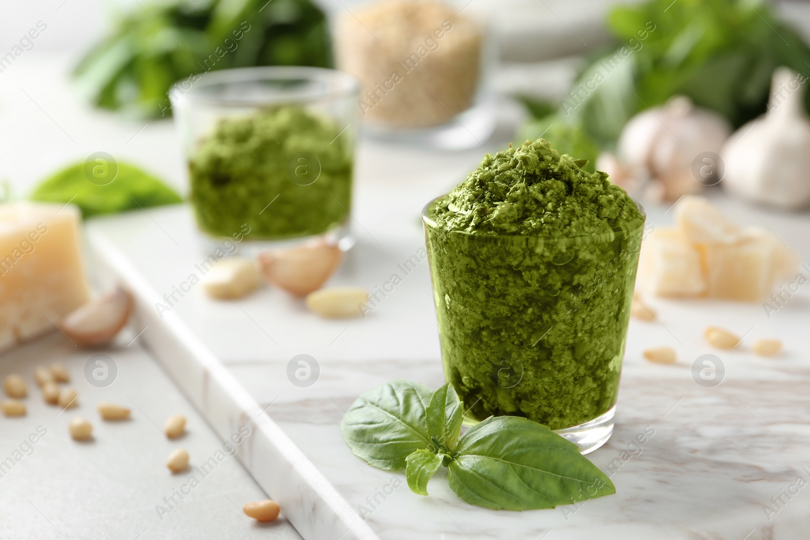 Photo of Board with glass of pesto sauce and basil on table. Space for text