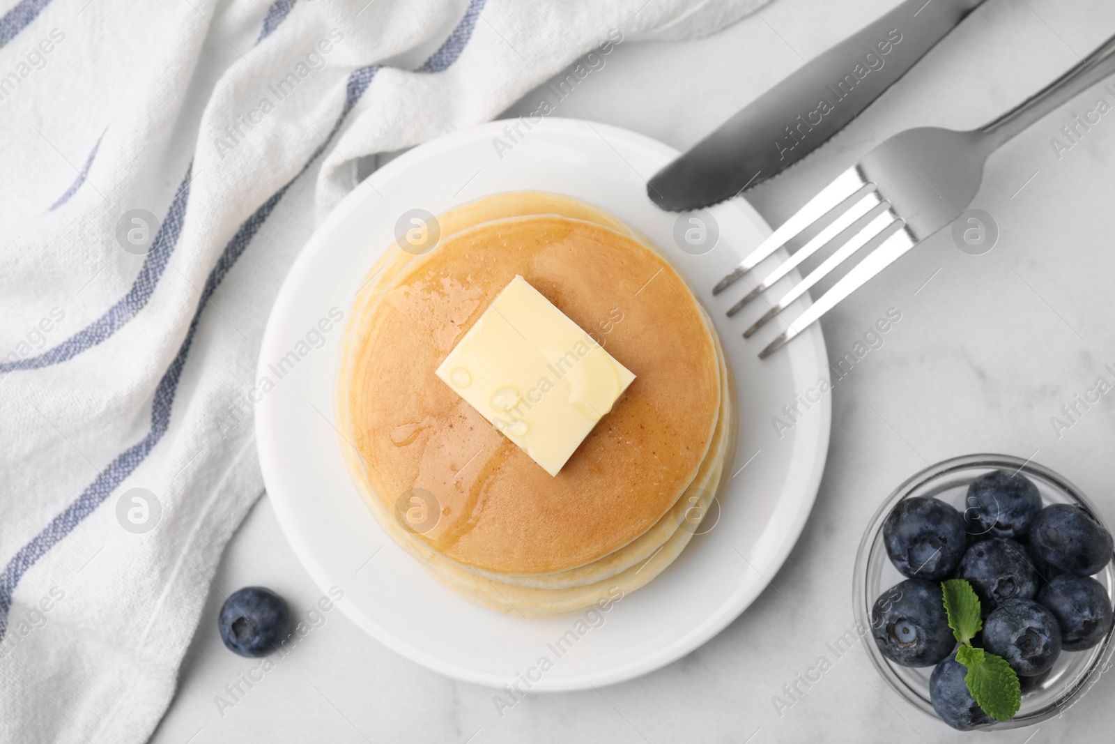 Photo of Delicious pancakes with butter and honey served on white marble table, flat lay