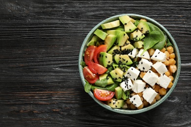 Photo of Delicious avocado salad with feta cheese on black wooden table, top view